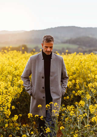 Portrait of a mature man in stylish gray jacket standing in a field surrounded by flowers. Conceptual of lifestyle, springの写真素材