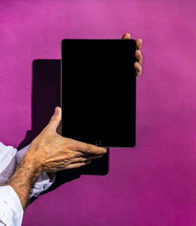 Unrecognizable person holding the empty screen of a tablet on a magenta or purple backgroundの写真素材