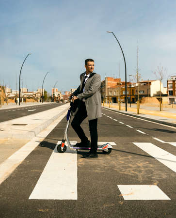 Elegant businessman in the city crossing the crosswalk on electric scooterの写真素材
