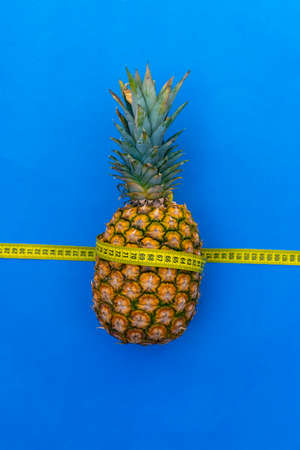 Pineapple wrapped with tape measure on blue backgroundの写真素材