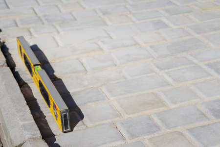 Defocus paving backyard patio background of stone floor texture. Yellow spirit level on paving stone footpath. Monotone light gray brick stone on the ground. Texture background. Pattern. Out of focusの写真素材