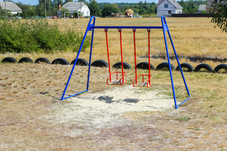 Defocus swing on playground on countryside area background. Bright blue and red swing. Family summer game. Out of focusの写真素材
