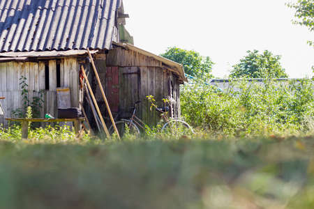 Defocused old dilapidated deserted barn in the courtyard on a green background. Various utensils near him. Old bike at the door. Simple rural life. out of focus.の写真素材