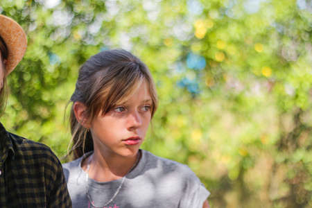 Defocused close-up preteen serious blond caucasian girl. Summer blurred green nature bokeh...