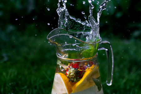 Defocus splash water bubbles in glass jug of lemonade with slice lemon, strawberry and mint on natural green background with water drops. Pitcher of summer cocktail mojito. Copy space. Out of focusの写真素材