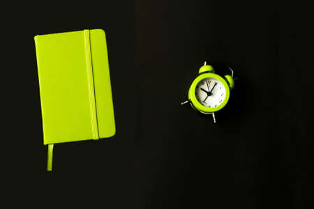 Directly Above Shot Of light green alarm clock with closed notepad Diary on black background. Time management concept. Back to school. Selective focus.の写真素材