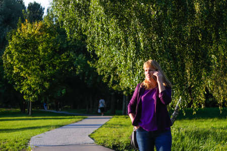 Defocus blond 40s woman standing in yellow autumn park. Happy beautiful lady. Women wearing gray pullover, yellow turtleneck, pendant, jeans. Fall park with leaves. Out of focus.の写真素材