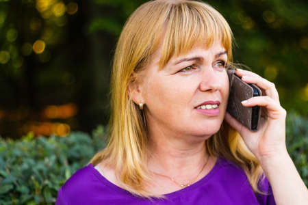 Defocus caucasian blond woman talking, speaking on the phone outside, outdoor. 40s years old woman...
