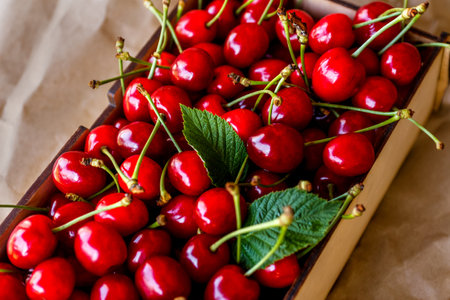 Close-up cropped box, crape of dark red sweet cherries with tail and leaves on craft wrinkled paper...