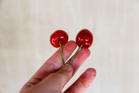 Defocus female hand holding and hanging two sweet cherries tail on craft old gray stone concrete...
