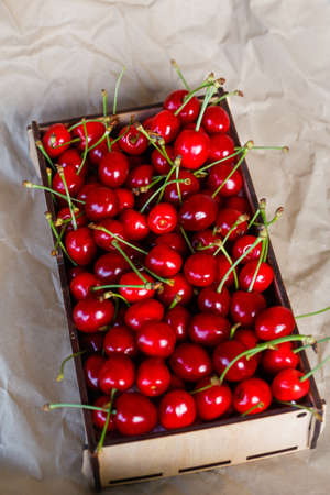 Wooden box, crape of sweet red cherries with tail and leaves on craft yellow wrinkled paper...
