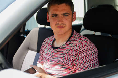 Serious successful caucasian young man sitting in car. 20s guy looking from open window. Silver gray...
