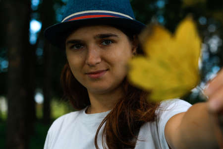 Defocus portrait of a happy young woman with brown hair wearing a hat outdoors. Female hand holding...
