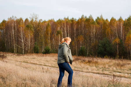 Defocus happy blond 40s woman standing in yellow autumn forest nature background. Happy beautiful lady. Women wearing purple sweater. Fall park, leaves. Dry grass, meadow. Out of focus.の写真素材