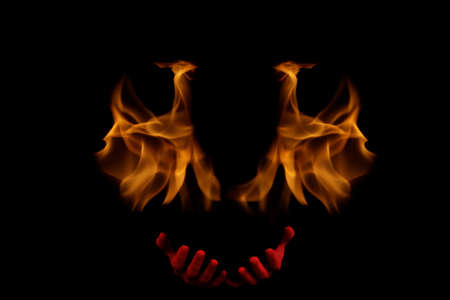 A silhouette of a man against the background of flames and fire stretches out red hands in blood. Begs and asks. Give up. Deadline is on. Halloween concept. Selective focus.の写真素材