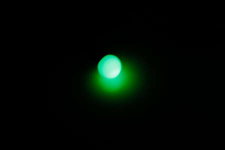One strong green blurred light. Green round light. Flashlight in the dark. Green round point of light. Festive mood. Give yourself the green light. Selective focus.の写真素材