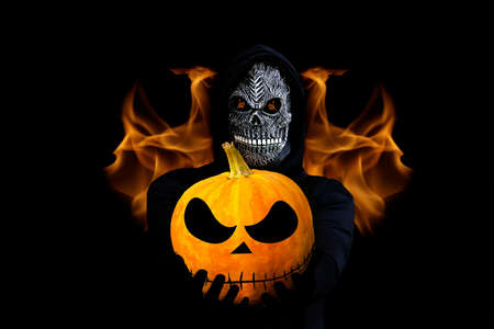Grim reaper holding halloween pumpkin head. Man in death mask with fire flame in eyes and grin on...