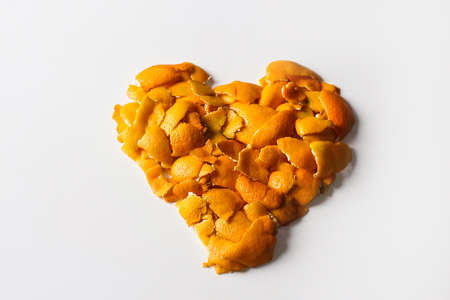 Close-up heart of dried orange and tangerine skins. On a white background. Lots of small pieces of dried orange peel laid out in the shape of a heart. Love symbol. Valentines Day. Selective focusの写真素材