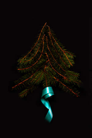 Xmas tree shape made of snowy fir branch with turquoise ribbon. Square composition, flat lay, view from above. Winter spruce concept. Vertical, black background. Selective focus.の写真素材