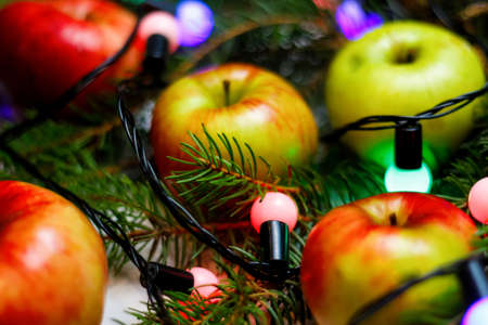 Many red and yellow organic apples on festive christmas tree background with bulb light. Food and diet. Healthy fruit background. Vitamin composition. Close-up. Blurred. Copy space.の写真素材
