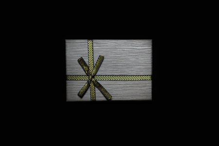 Defocus one gift with gold bow on dark black background. Horizontal with copy space. Gray male gift...