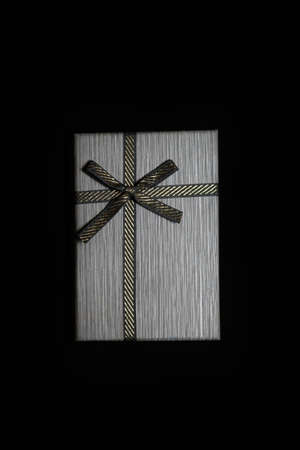 Defocus one gift with gold bow on dark black background. Horizontal with copy space. Grey male gift box for him, man, men, father. Luxury package present. Vertical. Out of focus.の写真素材