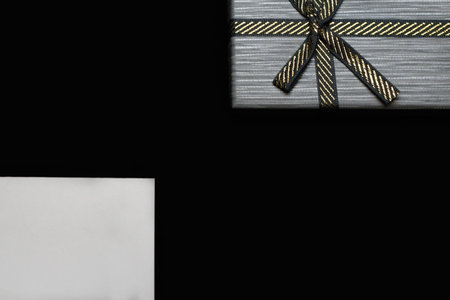 Defocus one gift with gold bow and blank white card on dark black background. Horizontal with copy space. Grey male gift box for him, man, men, father. Luxury package present. Out of focus.の写真素材