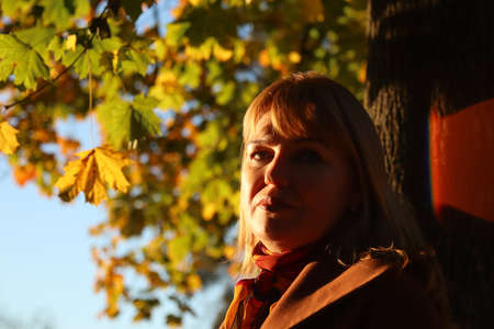 Portrait of candid young Caucasian blonde woman in colorful autumn park. Bright stylish woman in...