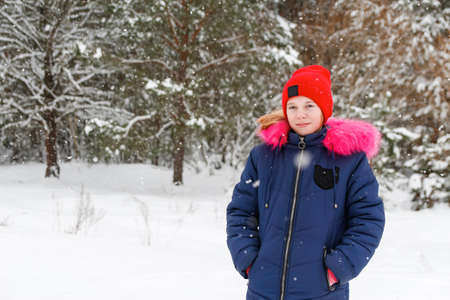 Portrait of preteen happy girl in red warm hat posing outside on nature winter snowy forest...