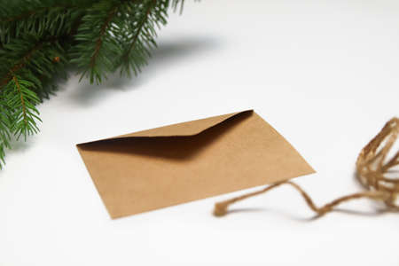 Craft eco envelope on white background. Christmas holiday concept. Letter to Santa Claus. Green natural background, fir tree branches. Simple rope.の写真素材