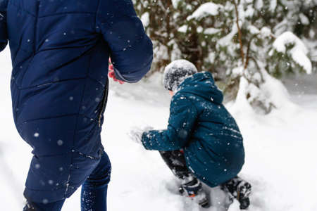 The boy swinging a snowball with a girl. Funny children in Winter forest playing snowballs, time...