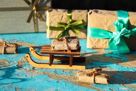 One wrapped craft vintage gift box lying wooden toy sled on blue old wooden background. Present box...