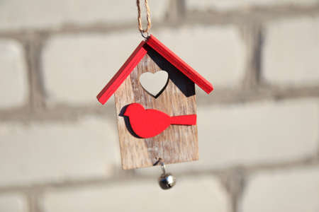 Wooden Christmas toy house with red roof and bird on white brick wall. Christmas decoration concept. Small house. Stay home. Mock-up for design.の写真素材