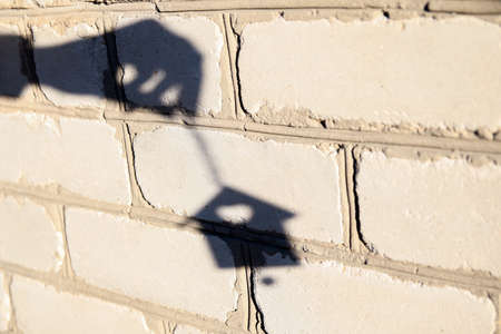 Defocus shadow of hand with Christmas toy small house on white brick wall. Light and shadow toy. House shadows with reflection on the house wall, outdoor, outside.の写真素材