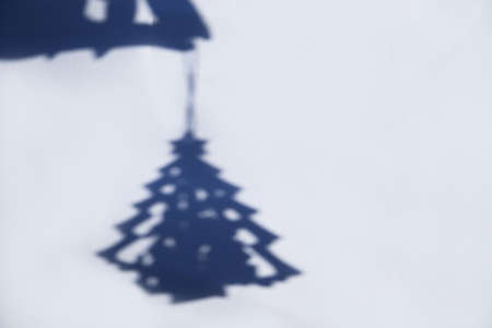Defocus blue Christmas tree toy. Shadow of hand with Christmas toy small christmas tree on white brick wall. Light and shadow toy. Shadows with reflection on the white textured background.の写真素材
