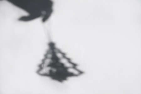 Defocus Christmas tree toy. Shadow of hand with Christmas toy small christmas tree on white brick wall. Light and shadow toy. Shadows with reflection on the white textured background Black and white.の写真素材