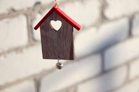 Love home concept. Wooden Christmas toy house with red roof on white brick wall. Christmas...