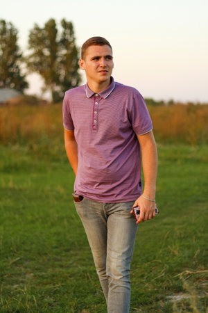 Young people.Portrait of serious young brunette man in purple polo shirt standing outdoor on nature background at summer day. 20s years guy. Millennial generation. Outside.の写真素材