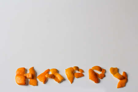 Defocus HAPPY word displayed by orange dry peel on a white background. Happiness concept. Greeting...