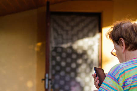 Old lady with wrinkled skin calling and speaking touchscreen smartphone. Nature background, close up, overhead, top view, copy space. selective focus.の写真素材