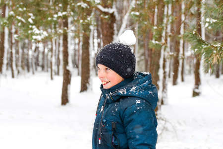 Defocus smiling child boy in winter forest in snowstorm with snowball on head. Funny kid on snowy...