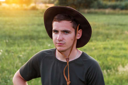 Young man farmer in cowboy hat at agricultural field on sunset with sun flare. Portrait of millennial man with hat, standing on nature background, outdoors in meadow. agriculture concept. copyspace.の写真素材
