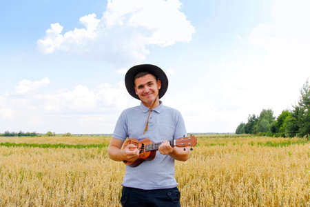 Young man smiling farmer in cowboy hat at agricultural field against blue sky. Portrait of millennial man standing on nature background, outdoors. Rancher on farmland. happy summer. close-up.の写真素材
