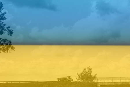War Ukraine. Ukrainian flag. A red tractor with a green trailer drives onto a bridge in the countryside in windy weather. You can see the grass, trees, cloudsの写真素材
