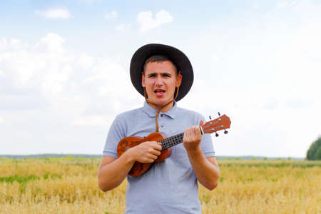 Guitar player. Young beautiful caucasian man playing ukulele outside. Handsome hipster guy plays...