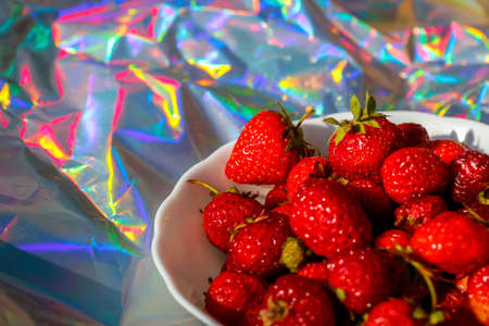Defocus close-up cropped bowl of ripe red strawberries on modern hologram background. Fruits and...