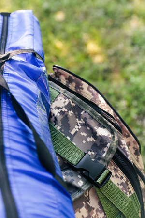 Defocus military backpack and blue tent or sleeping bag. Army bag on green grass background near tree. Military camouflage army rucksack. Tourist summer hiker. Summer. Close-up. Out of focusの写真素材