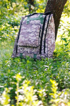 Defocus military backpack. Army bag on green grass background near tree. Military camouflage webbing...