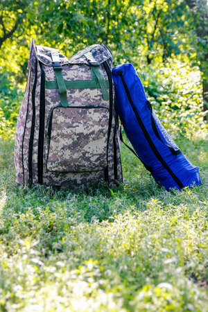 Defocus military backpack and blue tent or sleeping bag. Army bag on green grass background near...