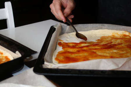 Defocus male hand make pizza dough with red tomato sauce. Homemade italian pizza. Base of Margarita. Home culinary. Men cooking and spreads the sauce by spoon. Out of focus.の写真素材